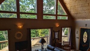 A spacious living room with a leather couch, wooden flooring, large windows, and a ceiling fan.
