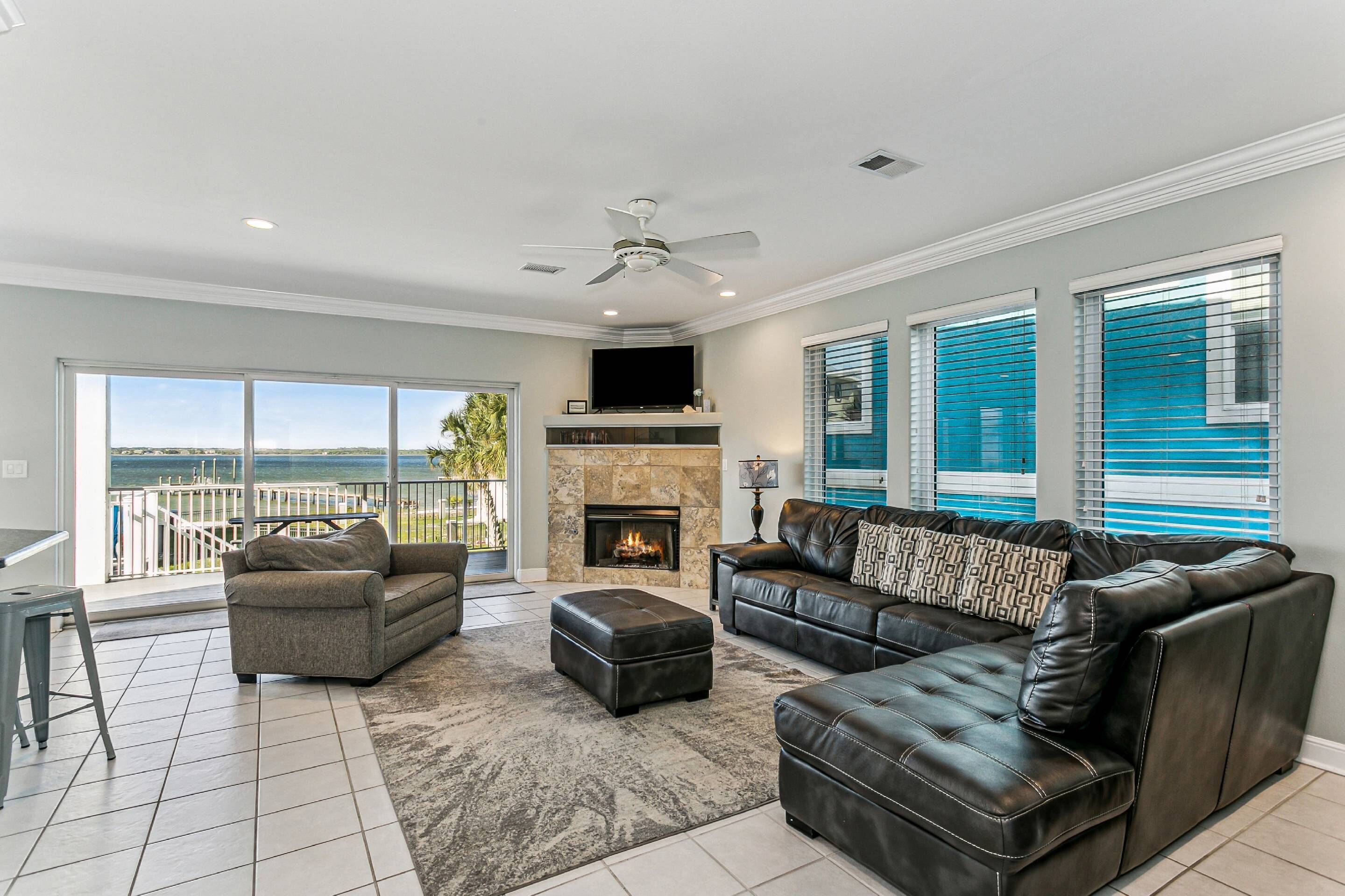 A spacious living room with a fireplace, leather sofas, a flat-screen TV, and a balcony with a view of the ocean.