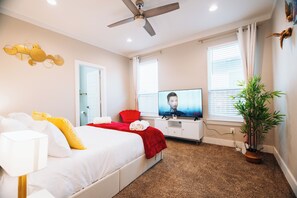 A hotel room with a bed, a television, a ceiling fan, a window with curtains, and a potted plant.