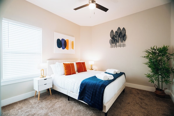 A neatly arranged bedroom with a bed, bedside tables, a ceiling fan, a wall art piece, and a potted plant. - Spacious 4-bedroom house with, Gameroom, Backyard, WiFi, AC in fabulous Dallas (Dallas)