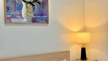 Habitación de hotel con cabecera de madera, cama con ropa blanca, mesita de noche con lámpara y un cuadro de flores en la pared.