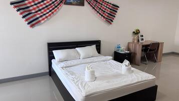 A neatly made bed with white linens and towels, a small bedside table with a lamp, and a desk with a chair.