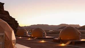 A desert landscape with multiple dome-shaped tents, each with a small attached structure, likely for amenities or services. - Siwar Luxury Camp  (Wadi Rum)