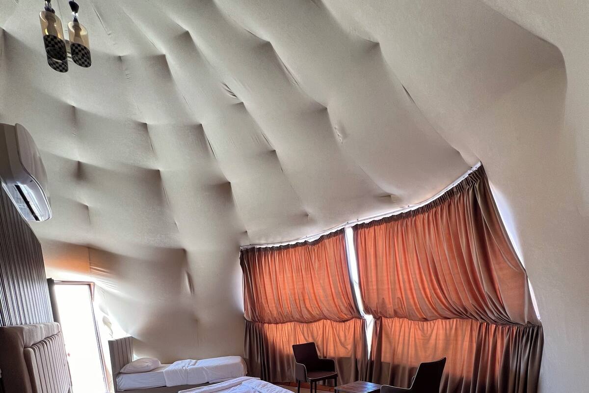 Une chambre d’hôtel moderne dotée d’un plafond au design original, de deux lits, d’une petite table et d’une chaise.