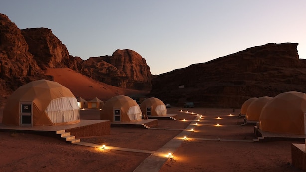 A desert landscape with multiple dome-shaped tents, each with a door and steps leading up to the entrance. - Siwar Luxury Camp  (Wadi Rum)