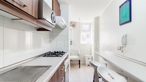 Uma cozinha moderna com fogão a gás, armários brancos e uma pequena área de jantar com uma cadeira e mesa brancas.