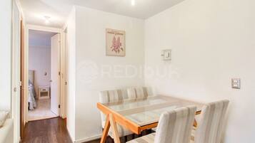 Un coin repas avec une table à plateau de verre et des chaises à rayures, un tableau encadré au mur et une porte donnant sur une autre pièce.