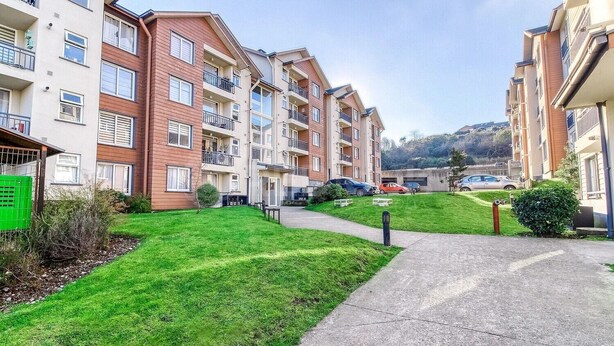 Um edifício residencial com várias varandas, um gramado verde e um caminho pavimentado.