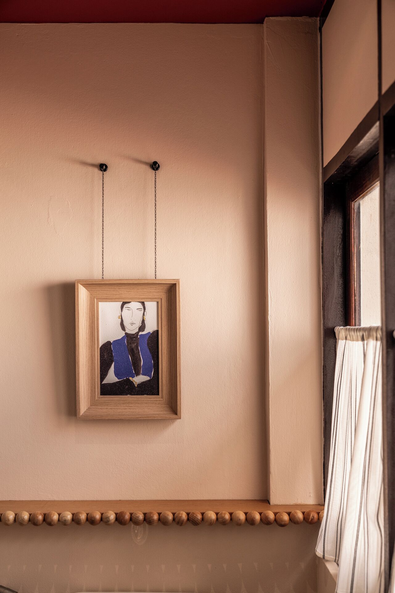A framed artwork hanging on a wall with a wooden shelf below.