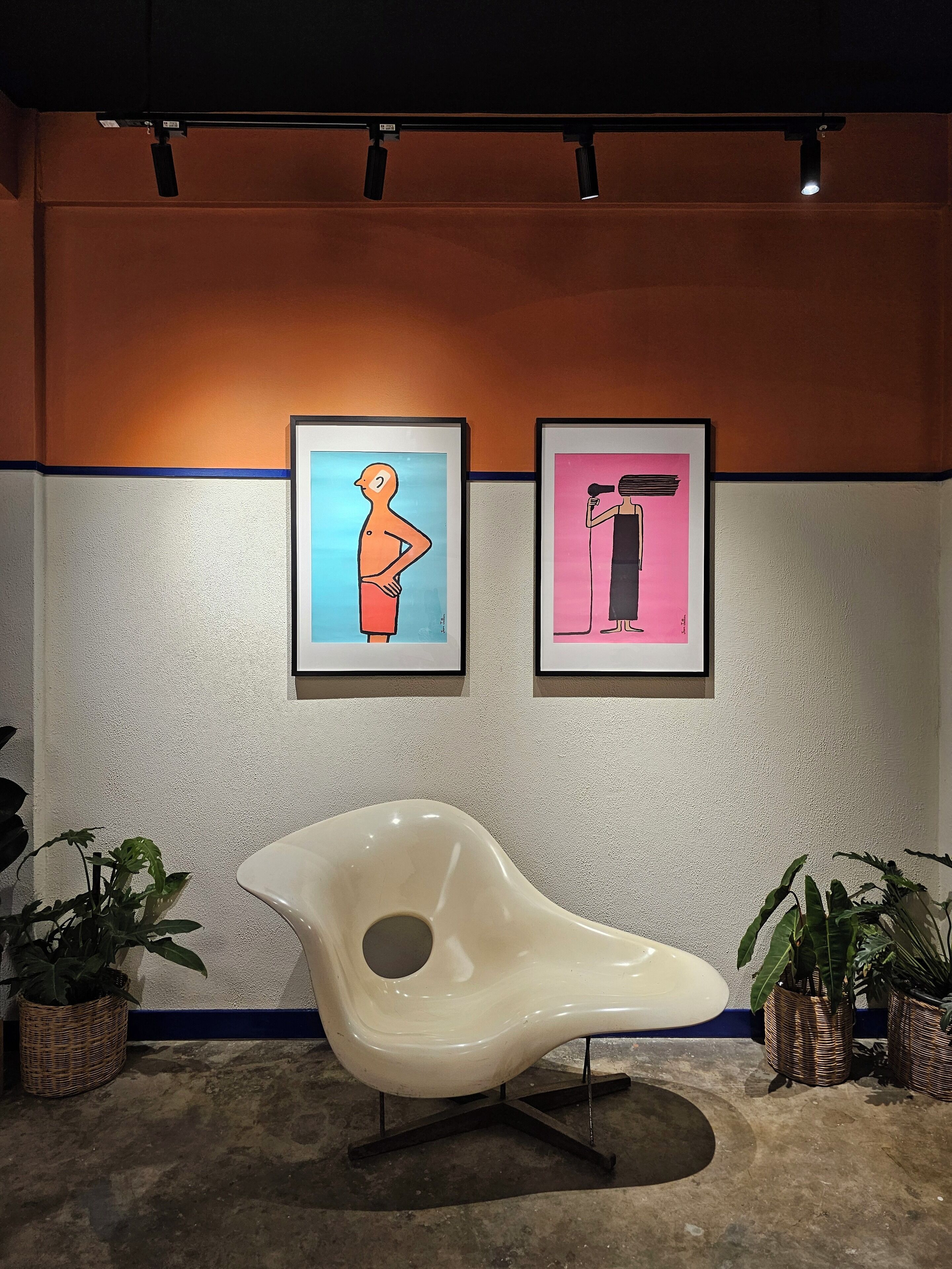 Un intérieur moderne avec deux œuvres d’art encadrées accrochées au mur, une chaise blanche originale et des plantes en pot.