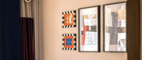 Habitación de hotel con dos camas, cabecero de madera, mesita de noche y dos obras de arte enmarcadas en la pared.
