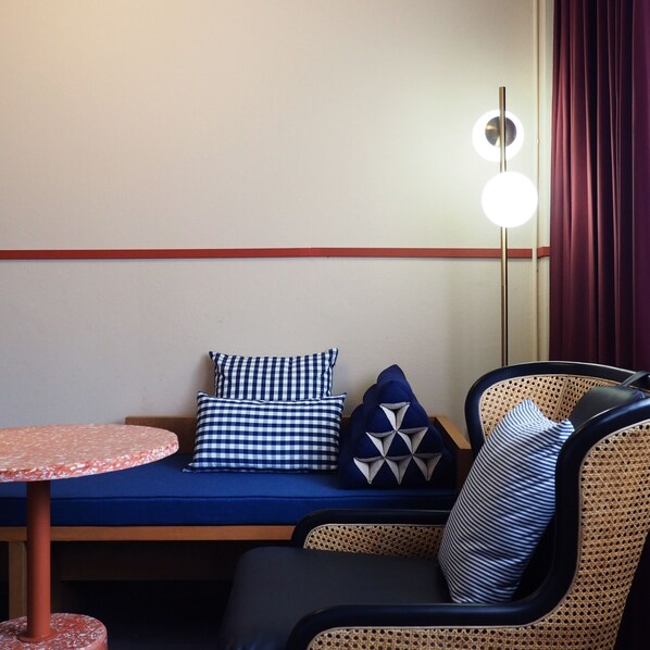 A seating area with a round table, a bench, and a chair with a woven backrest. - Blu Dock Restel Bangkok (Bangkok)