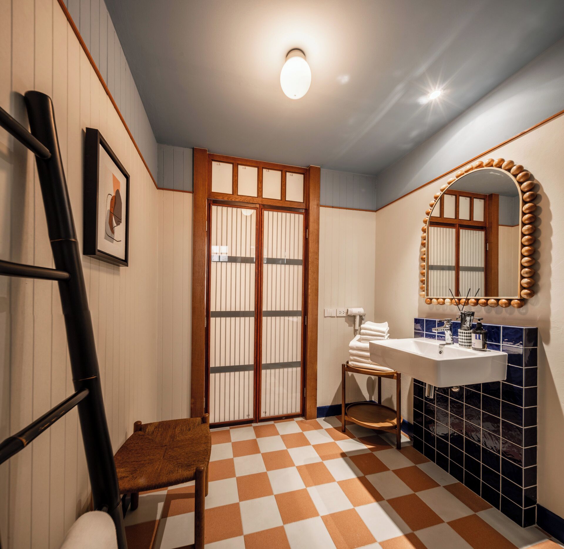 A bathroom with a checkered floor, a wooden chair, a sink with a mirror, and a toilet.