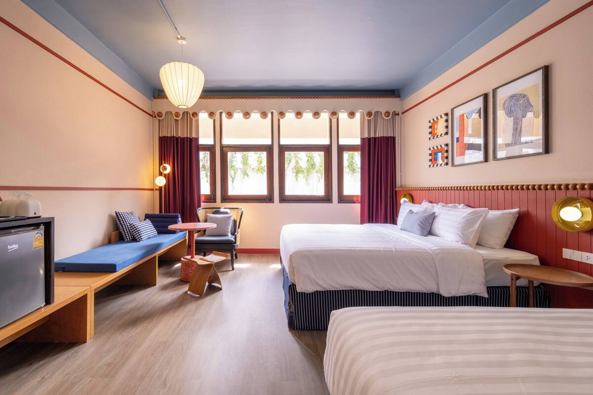A hotel room with a bed, a desk, a chair, a bench, and a window with curtains.