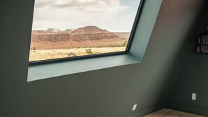 Een slaapkamer met dakraam, een bed met oranje dekbed en uitzicht op een woestijnlandschap.