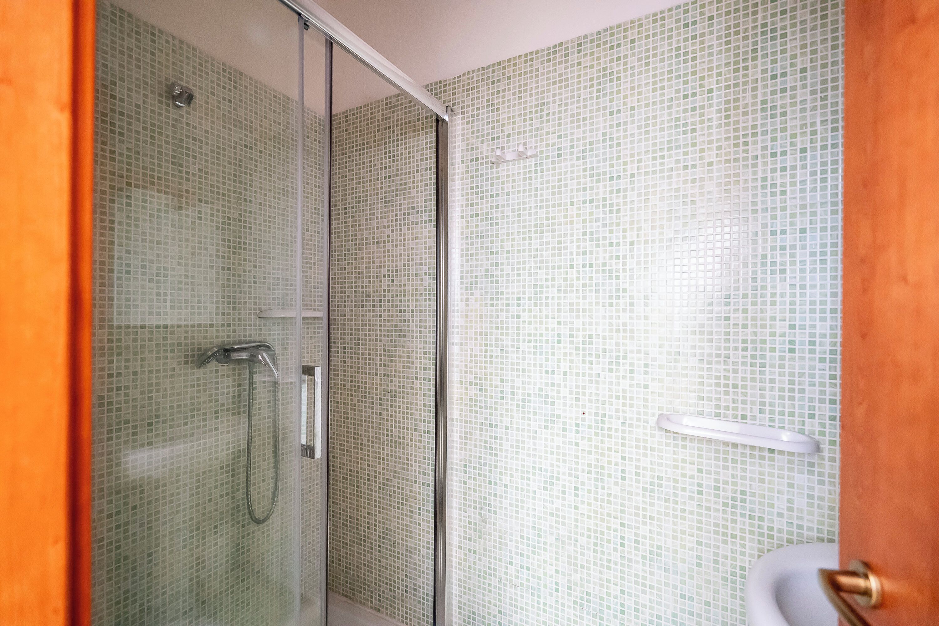 Une salle de bain avec une douche à parois de verre, des murs carrelés et un lavabo blanc.