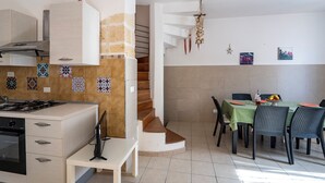 A modern kitchen with a built-in stove, a dining area with a table set for four, and a staircase leading to an upper level. - Villino Sole 1 Airco Near Beach & Centre (Porto Cesareo)