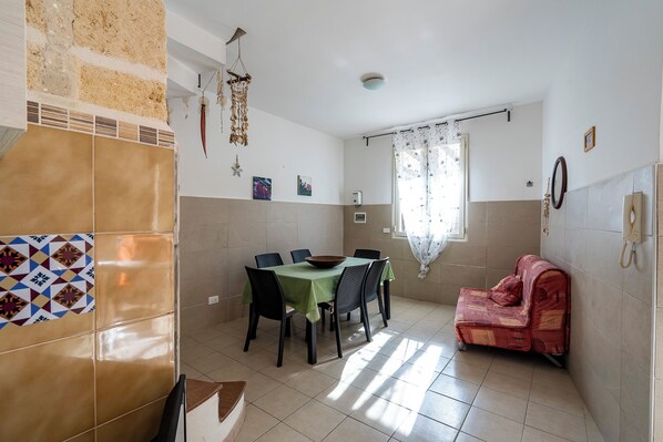 A dining area with a table and chairs, a sofa, a decorative wall, and a window with curtains.