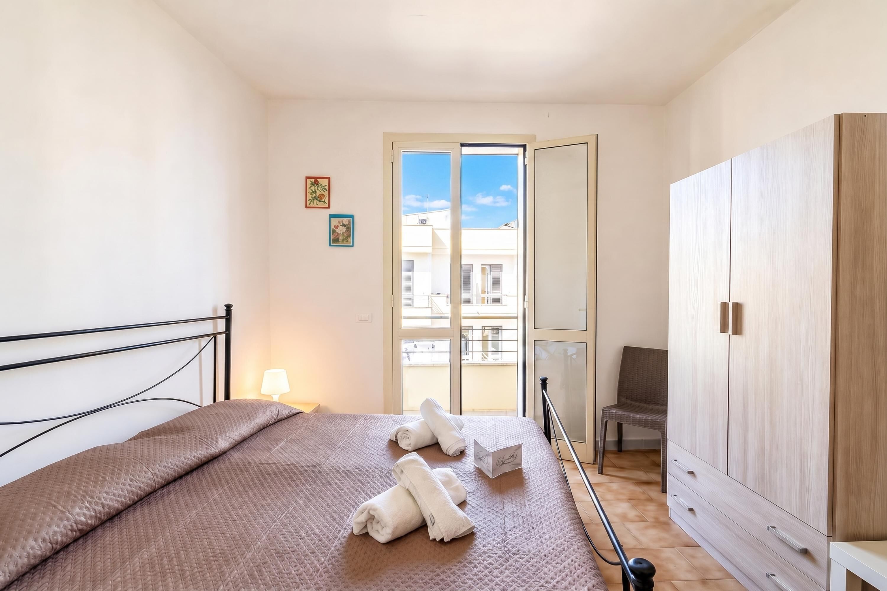 A bedroom with a bed, a wardrobe, a chair, and a balcony view.