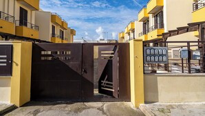 Una entrada protegida con reja metálica, edificios amarillos y cielo despejado.