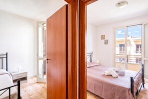 A bedroom with a bed, a nightstand, a wardrobe, and a balcony with a view of buildings. - Villino Sole 3 With A/C Near Beach & Centre (Porto Cesareo)