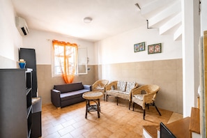 A modern living room with a sofa, two wicker chairs, a small round table, and a television. - Villino Sole 3 With A/C Near Beach & Centre (Porto Cesareo)