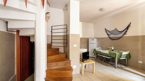 A staircase leading to a dining area with a table set for two, a television on a small table, and a hammock on the wall. - Villino Sole 4 Airco Near Beach & Centre (Porto Cesareo)