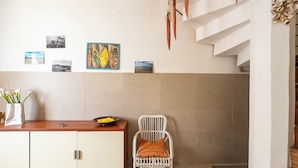 A kitchen with a white cabinet, a wicker chair, and a wall with framed pictures. - Villino Sole 4 Airco Near Beach & Centre (Porto Cesareo)