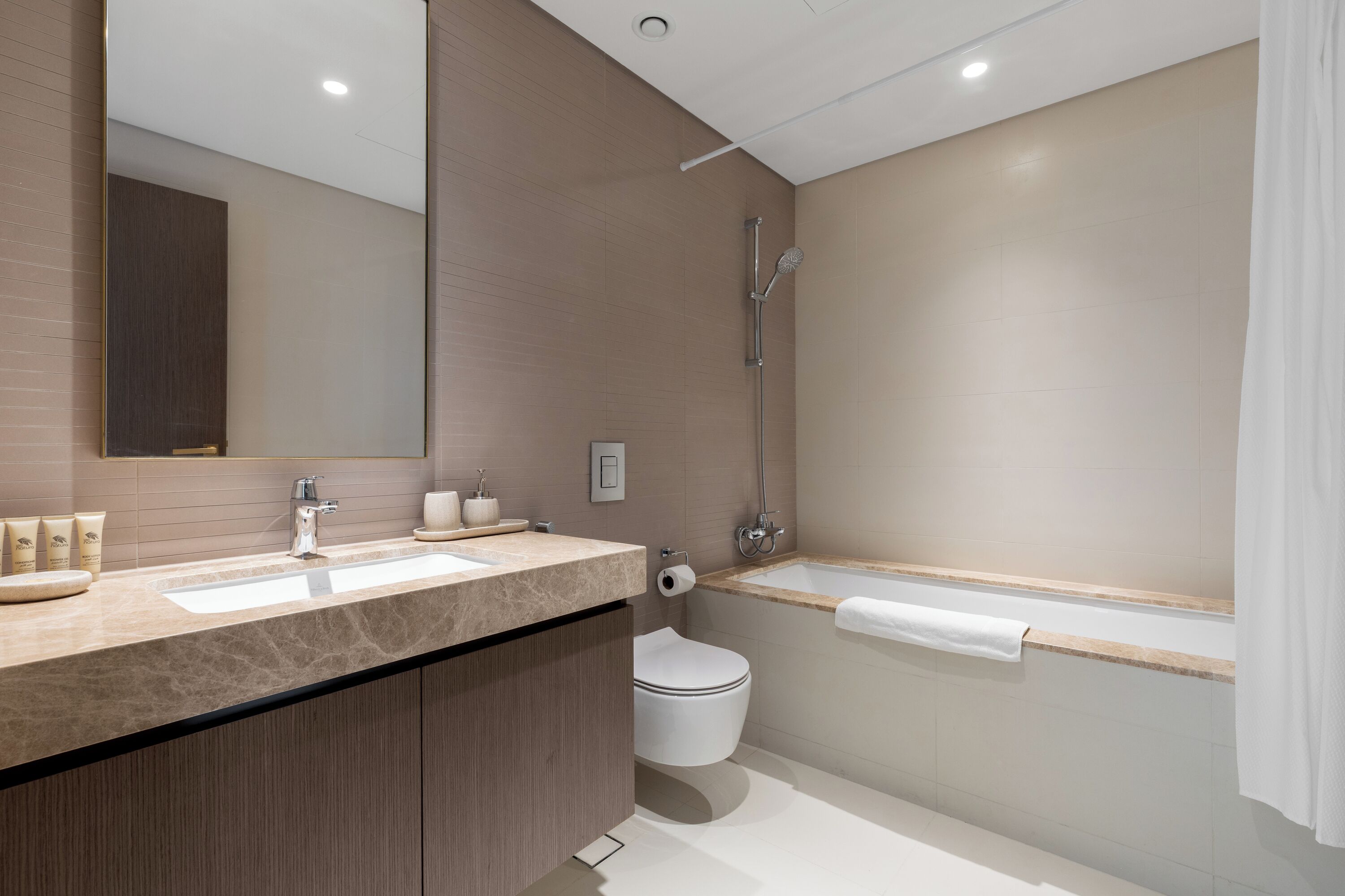 Une salle de bain moderne avec un grand miroir, un lavabo, des toilettes et une baignoire.