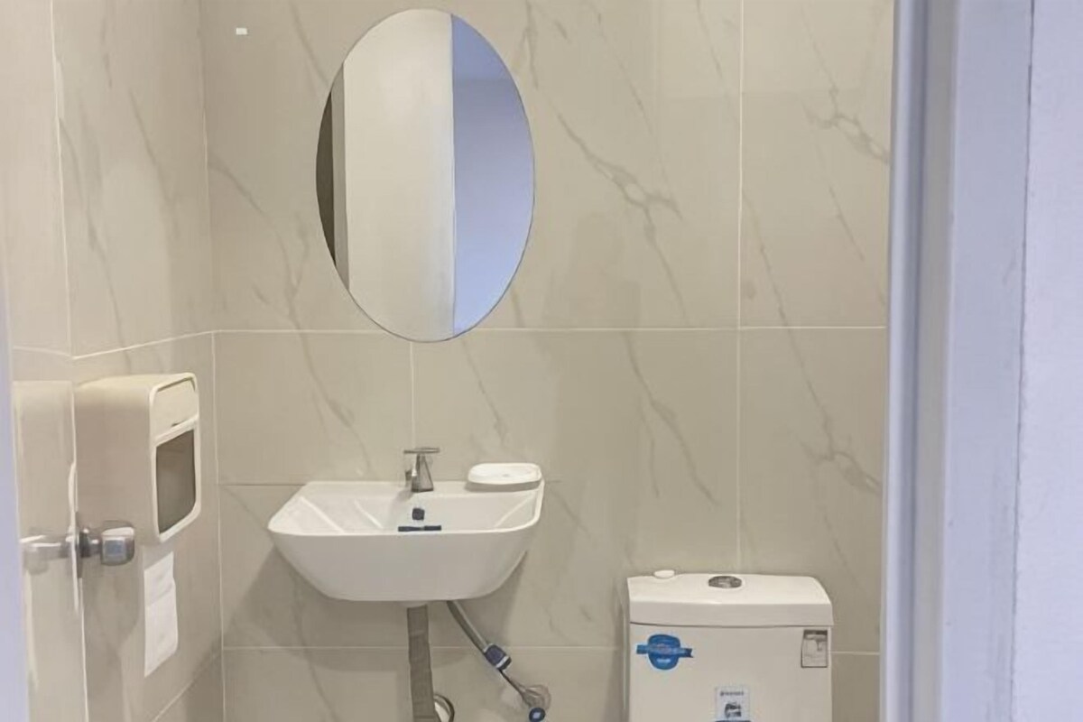 A bathroom with a white sink, a toilet, a mirror, and a soap dispenser.