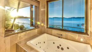 Ein modernes Badezimmer mit einer großen Badewanne, Seeblick und einem Fenster mit Jalousien.