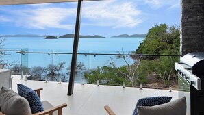 Eine Terrasse mit Meerblick, einem Grill und Sitzgelegenheiten mit gemusterten Kissen.