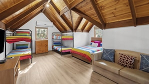 Une chambre de dortoir avec des poutres en bois, des lits superposés, un bureau et un canapé.