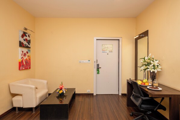 A room with a white sofa, a wooden coffee table with a vase of flowers, a desk with a mirror, and a door with a sign. - THE Woodrose (Bengaluru)