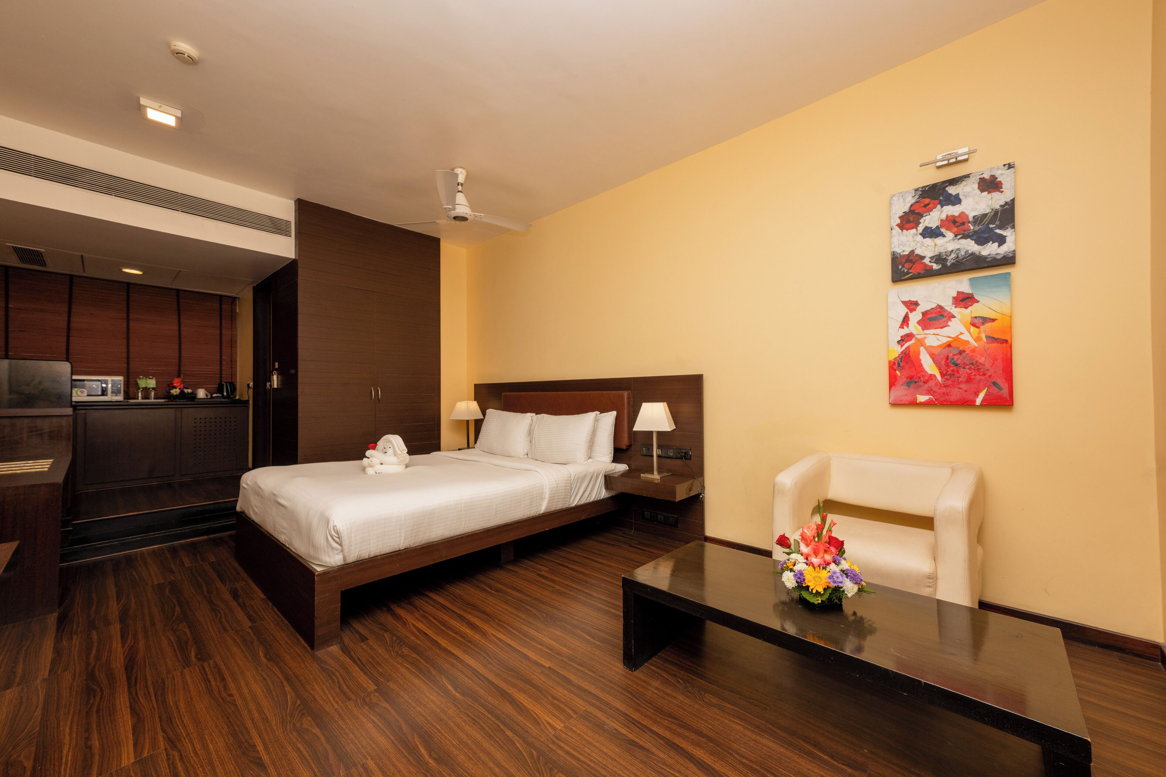 A hotel room with a bed, bedside tables, a desk, a chair, and artwork on the wall.