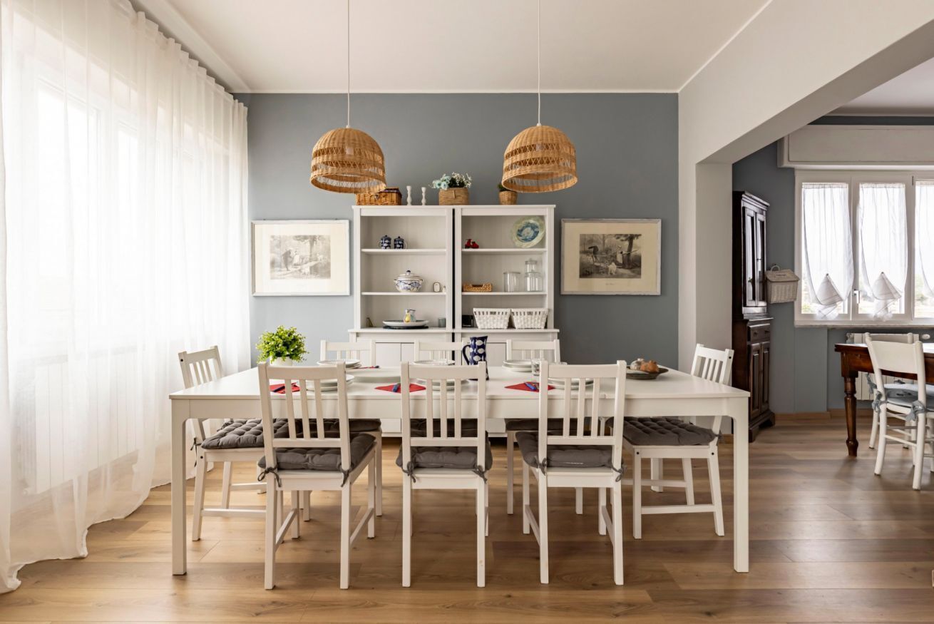 A dining area with a white table and chairs, a white cabinet with shelves, and two hanging wicker lamps.