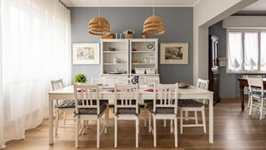 Un coin repas avec une table et des chaises blanches, un meuble blanc avec des étagères et deux lampes suspendues en osier.