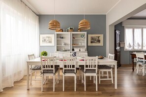 A dining area with a white table and chairs, a white cabinet with shelves, and two hanging wicker lamps.