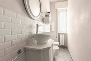 A bathroom with white subway tiles, a white sink, a round mirror, and a toilet.