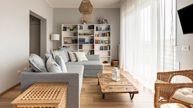 Un salon comprenant un canapé, une table basse, une bibliothèque et un fauteuil en osier.