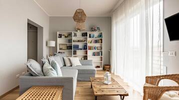 Una sala de estar con sofá, mesa de centro, estantería y una silla de mimbre.