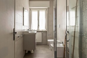 A bathroom with a toilet, sink, and shower area, featuring a window and patterned tiles.