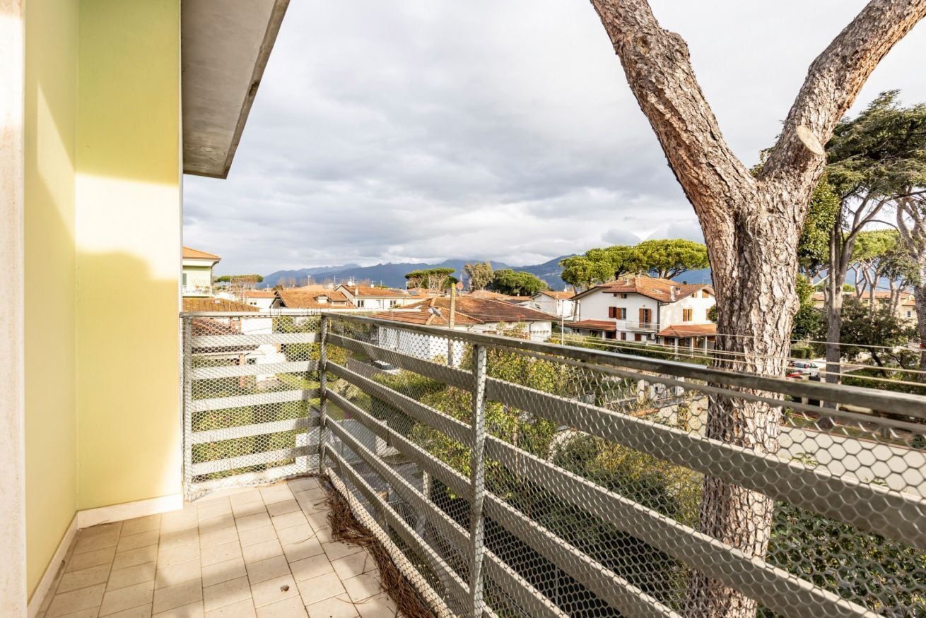 Un balcón con barandilla de metal que da a una zona residencial con casas y árboles.