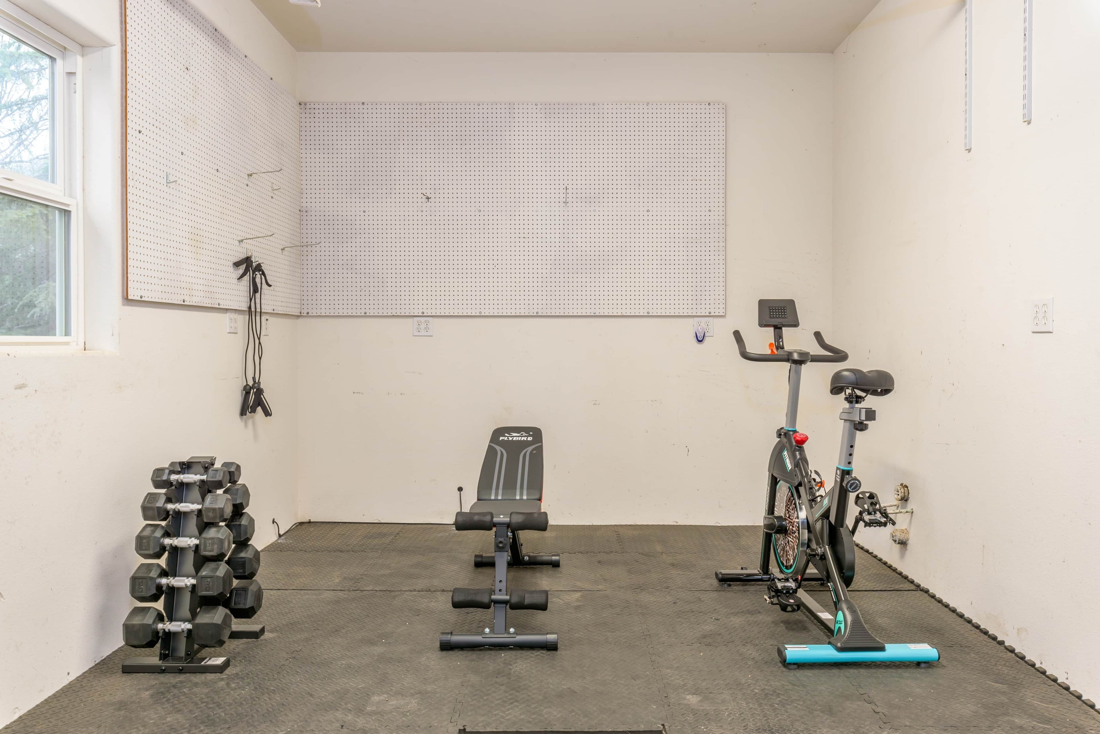 A gym with a wall-mounted pegboard, a bench, a bike, and a rack of dumbbells.