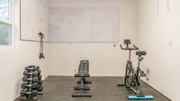 A gym with a wall-mounted pegboard, a bench, a bike, and a rack of dumbbells.