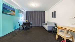 A room with a dining table, chairs, a sofa, a TV mounted on the wall, and a window with curtains.