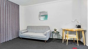 Una sala de estar moderna con un sofá gris, una mesita de madera con una silla, una lámpara y una planta en maceta.