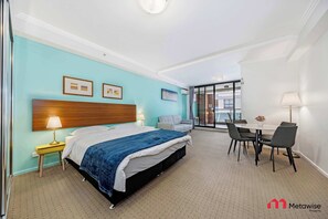 Ein Hotelzimmer mit Bett, Nachttisch, Lampe und einem Essbereich mit Stühlen und Tisch.