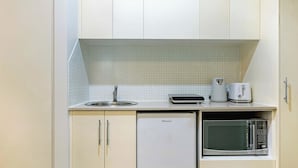 Una kitchenette compacta con un lavamanos, una cafetera, un tostador y un microondas.