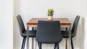 Una pequeña mesa de comedor con tapa de madera y dos sillas negras. Hay una planta en maceta sobre la mesa.